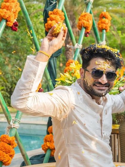 The groom enjoying his Haldi ceremony, posing playfully for the camera against a poolside backdrop decorated with marigolds.
