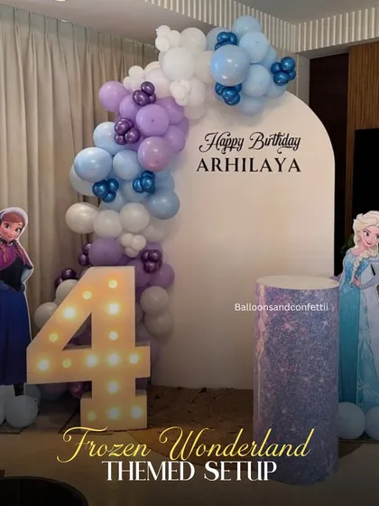 A magical Frozen wonderland for a 4th birthday. The setup includes an icy-toned balloon garland, character cutouts of Anna and Elsa, and a light-up marquee number.