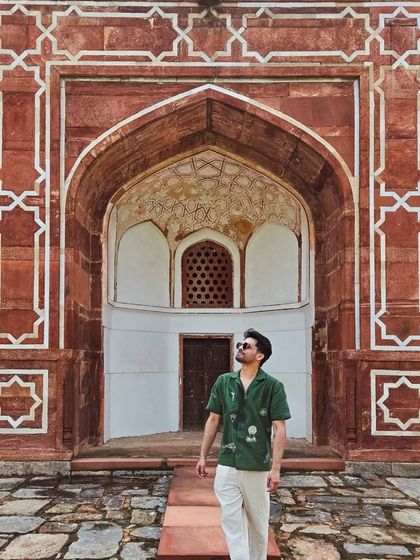 Standing before a grand archway at Humayun's Tomb, the intricate red sandstone and marble patterns creating a perfect frame.