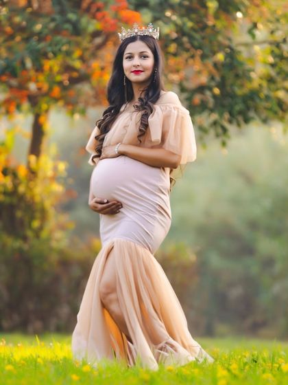 A regal outdoor portrait of an expectant mother wearing a crown and a fitted mermaid gown. The golden hour light in the park gives her a beautiful, warm glow.