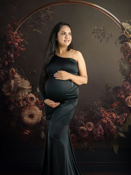 A beautiful portrait of a mom-to-be in a sleek black gown, looking thoughtfully to the side, framed by a floral ring.