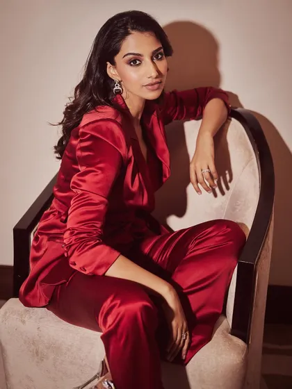 A seated portrait in the red satin pantsuit, exuding confidence and modern elegance. The styling is sharp and polished from head to toe.