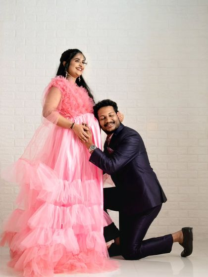 A classic pose for a maternity photoshoot, made even more special with our coordinated outfits. The expecting mother is wearing a beautiful pink ruffled gown, while her partner's suit complements her look perfectly.