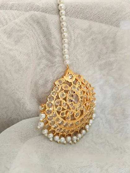 The 'Ujwala' Hyderabadi Jadau Mangtika. This piece features a beautiful crescent shape with intricate filigree work and pearl drops.