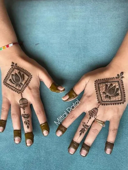 A unique back-hand design featuring a lotus motif in a diamond-shaped frame with hanging details. This is a great example of a modern, jewelry-inspired henna design.