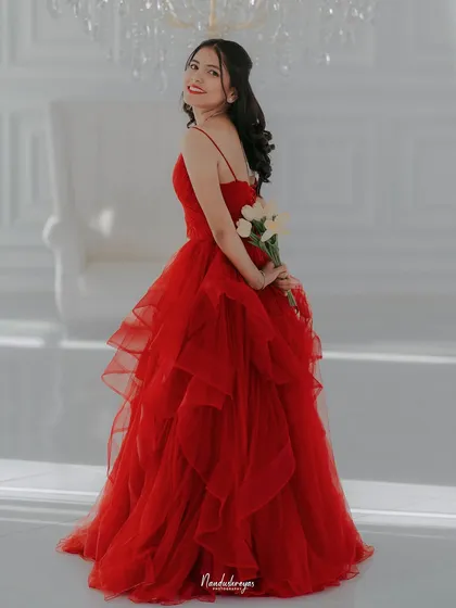 A beautiful solo portrait of the bride-to-be in a vibrant red gown, holding flowers behind her back in a bright, all-white studio.