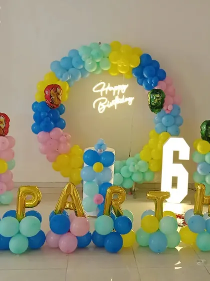 A colorful superhero-themed 6th birthday party with a circular balloon arch and character foils.