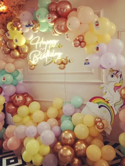 A magical unicorn and pastel rainbow theme for a child's birthday. This full backdrop is filled with balloons in soft colors, a unicorn cutout, and a "Happy Birthday" neon sign to complete the look.
