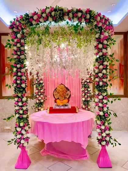 An elaborate and beautiful floral mandap for Ganpati, using a full arch of artificial pink and white roses and hanging wisteria to create a grand and festive look.