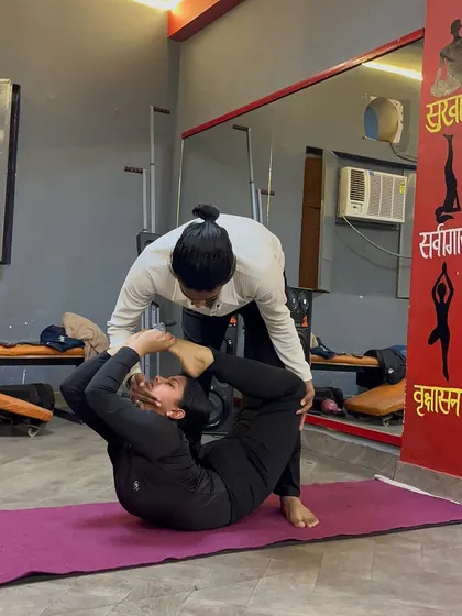 Continuing the adjustment in a deep back-bending pose, helping the student to bring their feet closer to their head.