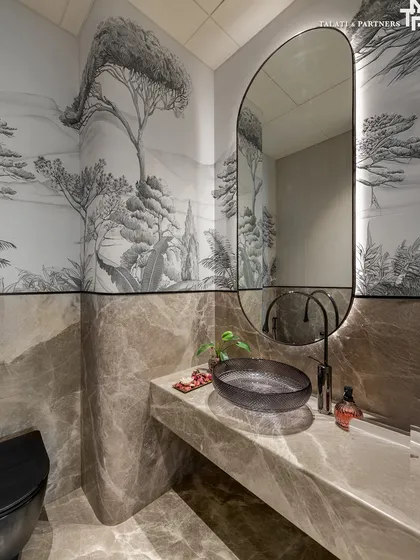 A powder room that offers a quaint sanctuary, embellished in marble and complemented by a greyscale scenic wallpaper. The subtle artisanal details, like the curved vanity and unique basin, echo a larger narrative of the home's design language.