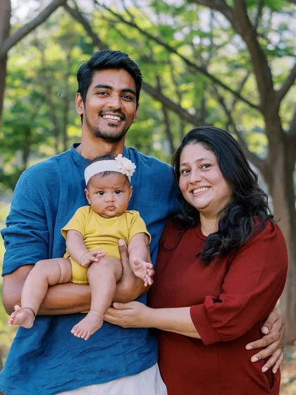 A happy family portrait taken outdoors, with the baby in a bright yellow outfit, perfect for celebrating a sunny festival day.