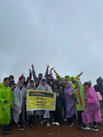 A happy group in colorful ponchos posing with our banner at the top of Netravathi peak.