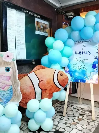 The entrance decoration for a mermaid party, featuring a welcome sign, a mermaid cutout, and a large clownfish prop, all tied together with blue balloon clusters.
