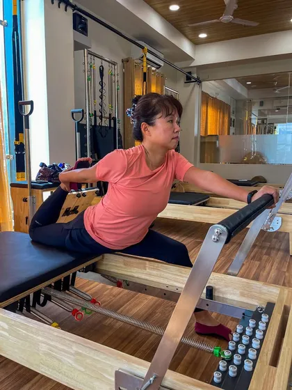 A client holds a deep pigeon stretch on the Reformer. Using the machine allows for a more supported and effective stretch to release tight hips, which can often contribute to lower back pain.