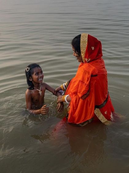 A mother and child share a moment of joy in the holy water during Chhath Puja, a candid photograph capturing the blend of ritual and family life.