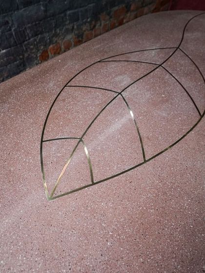 A close-up of a custom terrazzo tabletop with a brass leaf inlay. The contrast between the warm, earthy red terrazzo and the sharp, metallic lines of the brass creates a stunning visual effect.