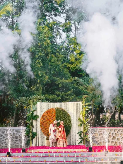 The couple exchanges varmalas amidst clouds of smoke and fireworks, a dramatic and spectacular moment at their farmhouse wedding.