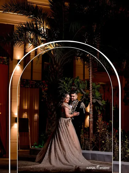 An elegant outdoor portrait at an evening engagement party. The archway frames the couple beautifully, and the lighting creates a sophisticated and opulent mood.