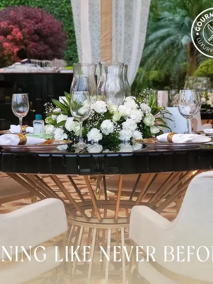 "Dining Like Never Before." A close-up of a perfectly set table with white flowers and elegant glassware, promising a unique and elevated dining experience.