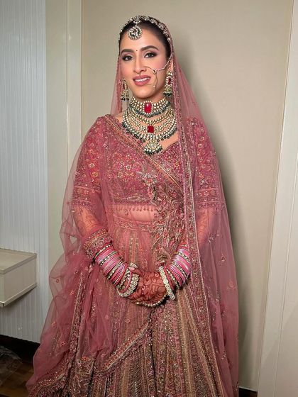 The full view of this stunning pink bridal lehenga, with makeup that is both modern and timeless, featuring a defined eye and radiant skin.