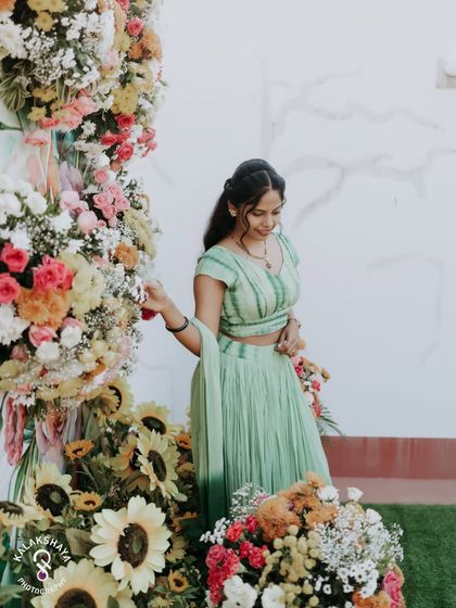 A beautiful shot of the bride posing with a large floral arrangement at her Haldi ceremony.
