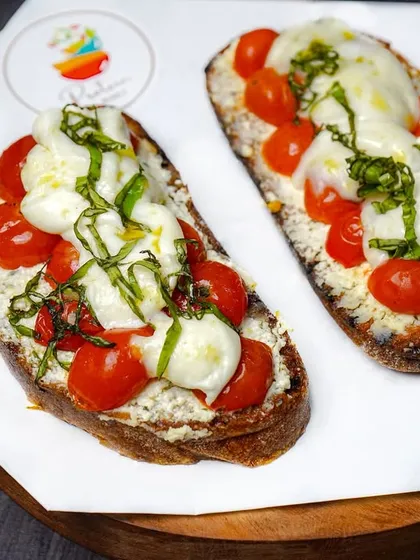 Fresh caprese bruschetta with cherry tomatoes, mozzarella, and basil on a dark wooden board. The contrast between the bright toppings and the dark background is visually striking.