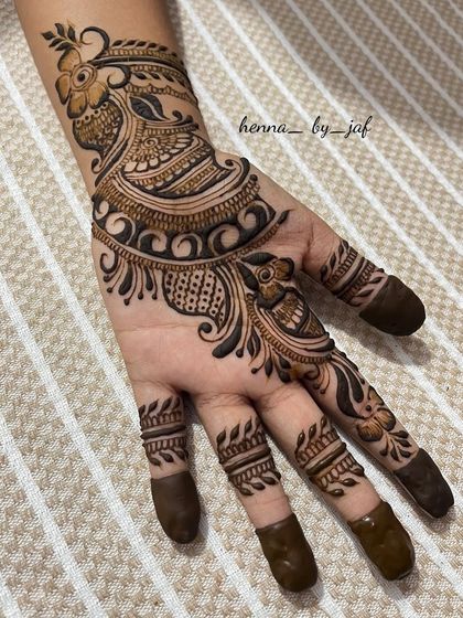 A classic Indian bridal design featuring a prominent peacock motif on the back of the hand. The fingers are fully covered with henna, and the wrist has a detailed band, perfect for a bride.