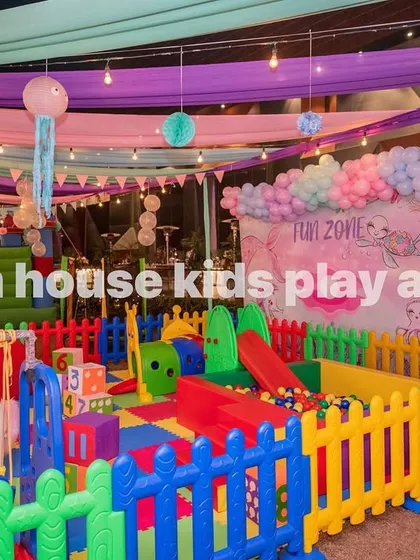 A 14x14 feet rainbow kids play area set up indoors under festive decorations. This view highlights the colorful soft flooring, fencing, and a variety of play structures like a slide and unicorn rocker.