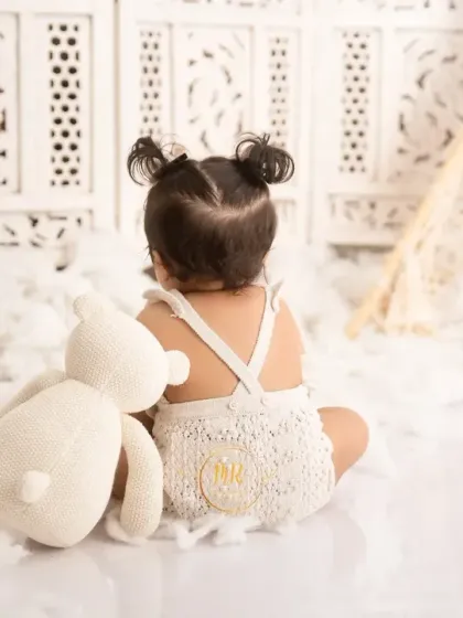 A quiet moment from behind, showing a baby girl with her teddy bear, highlighting her cute pigtails and knitted romper.