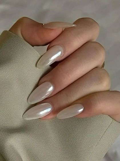 A pearlescent, off-white manicure on long, almond-shaped nails, perfectly complementing a neutral outfit. This shows the versatility of 'glazed' nails.