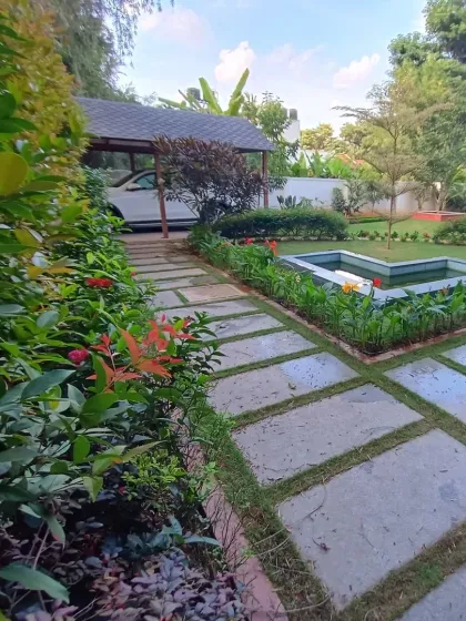 A closer look at the stone pathway and a geometric pond feature. The path is flanked by flowering shrubs, adding color and texture to the garden walk.