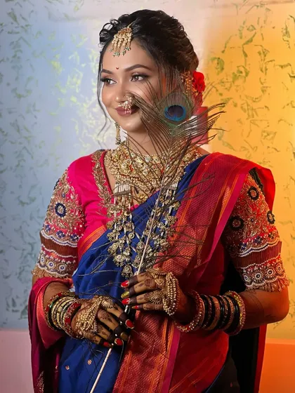 A creative shot of a bride in a blue Paithani, holding a peacock feather that complements her saree's colors.