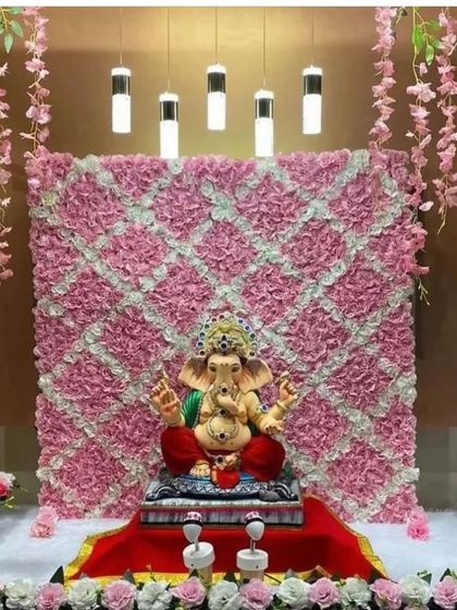 A simple yet elegant Ganpati backdrop made from a patterned wall of pink and white flowers. The clean lines and modern lighting make this a sophisticated choice for a home celebration.