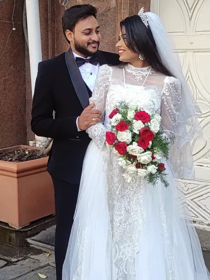A beautiful moment from a Christian wedding. Our bride is wearing a delicate lace gown with long sleeves and a full tulle skirt, complemented by the groom's classic black tuxedo. I help couples find perfectly coordinated outfits for their special day.