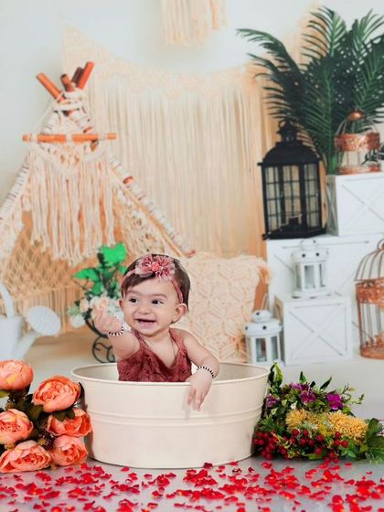 A playful moment as a baby girl reaches out from her tub in a boho-themed splash session. The flowers and lanterns create a warm and inviting atmosphere.