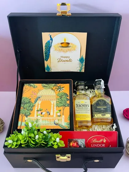 A sophisticated Diwali hamper for him. This black suitcase box contains miniature whiskey bottles, Lindt chocolates, and a beautiful notebook.