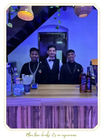 Three of our professional bartenders posing behind a rustic wooden bar. Their smart attire and confident stance reflect the high standards of service we provide for all types of events.