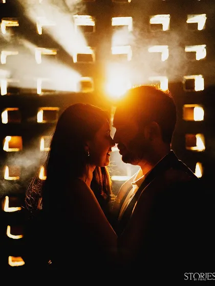 A beautiful silhouette created by the setting sun. The light filtering through the grid behind them creates a warm, atmospheric glow, highlighting their profiles in a moment of intimacy.