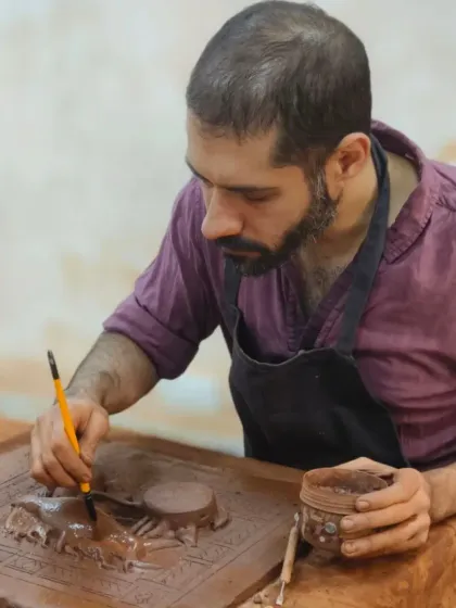 A student meticulously works on a detailed relief sculpture. Using fine tools, he carves and shapes the clay to create intricate patterns and forms, showcasing advanced sculpting techniques.