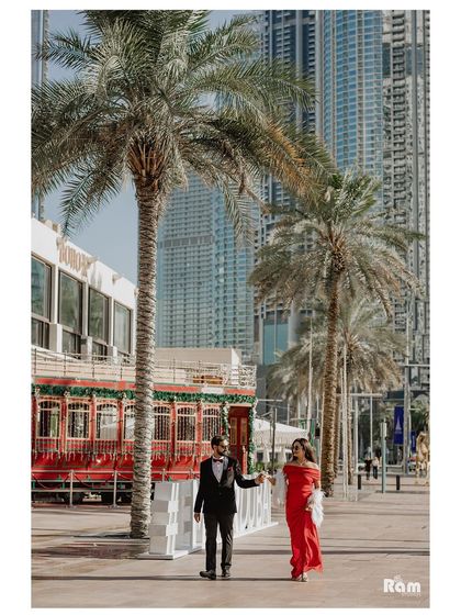 A candid shot of the couple walking through downtown Dubai, with the city's modern architecture and a classic red trolley in the background. This image blends romance with an urban vibe.