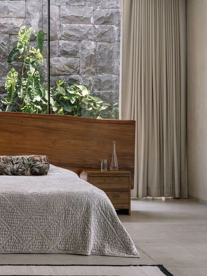 A closer look at the master bed, with its custom live-edge headboard and the view of the stone-clad courtyard wall. This composition perfectly illustrates our modern organic design philosophy.