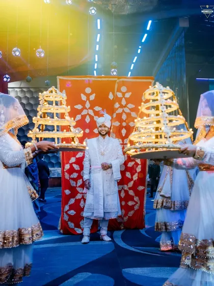 The groom's grand entrance, flanked by attendants with ornate lamps, creating a regal and traditional welcome.