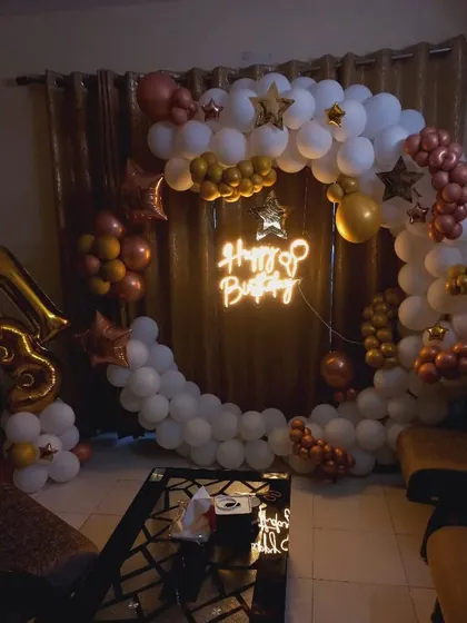 A cozy and elegant 13th birthday decoration at home. The ring is decorated with white, gold, and rose gold balloons, with a 'Happy Birthday' neon sign in the center.