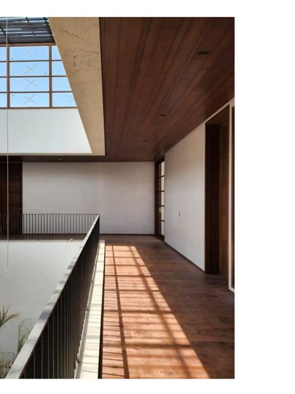 A corridor in the Ishtika house, with warm wood flooring and a view down into the central, multi-level courtyard. The play of light from the slatted roof above creates a dynamic, ever changing pattern on the floor.