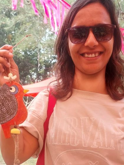 A happy customer at the Goa Potter's Fest holding a red robin chime. These bird-themed bells are perfect for adding a touch of whimsy to a garden or balcony.