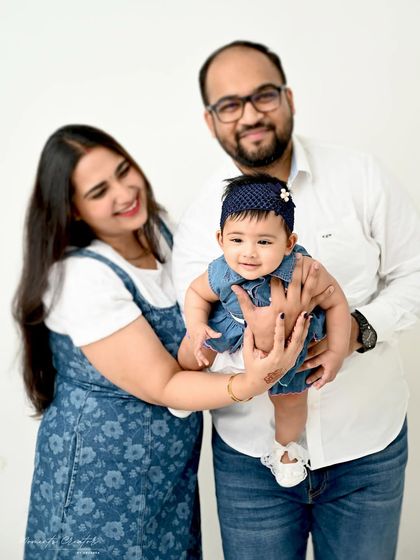 A playful moment as parents lift their smiling baby girl. The simple white background emphasizes the pure joy and connection in this family portrait.