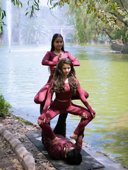 A three-person acroyoga totem pole pose, set against a beautiful park backdrop. This is a great example of a visually impressive team pose.