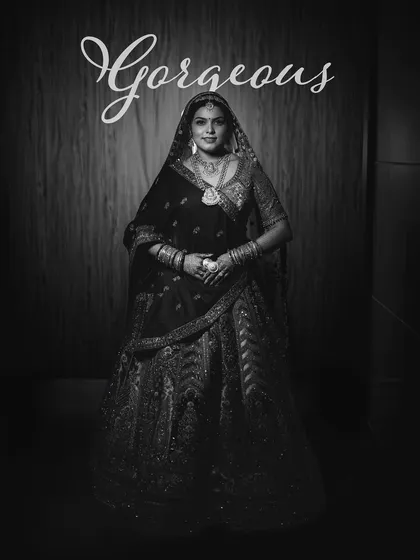 A gorgeous full-length bridal portrait in black and white, emphasizing the bride's regal stance and the intricate work on her traditional lehenga.