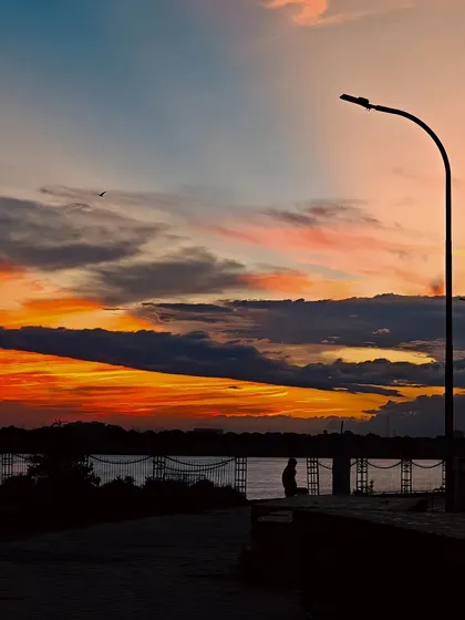 A stunning sunset silhouette at Ganga Barrage in Kanpur, with a lone figure and a lamppost against a colorful sky.